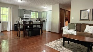 A spacious living area with a wooden dining table, a sofa, and a kitchen with green cabinets and white appliances. - Low Key Living Hideaway (Lavalette)