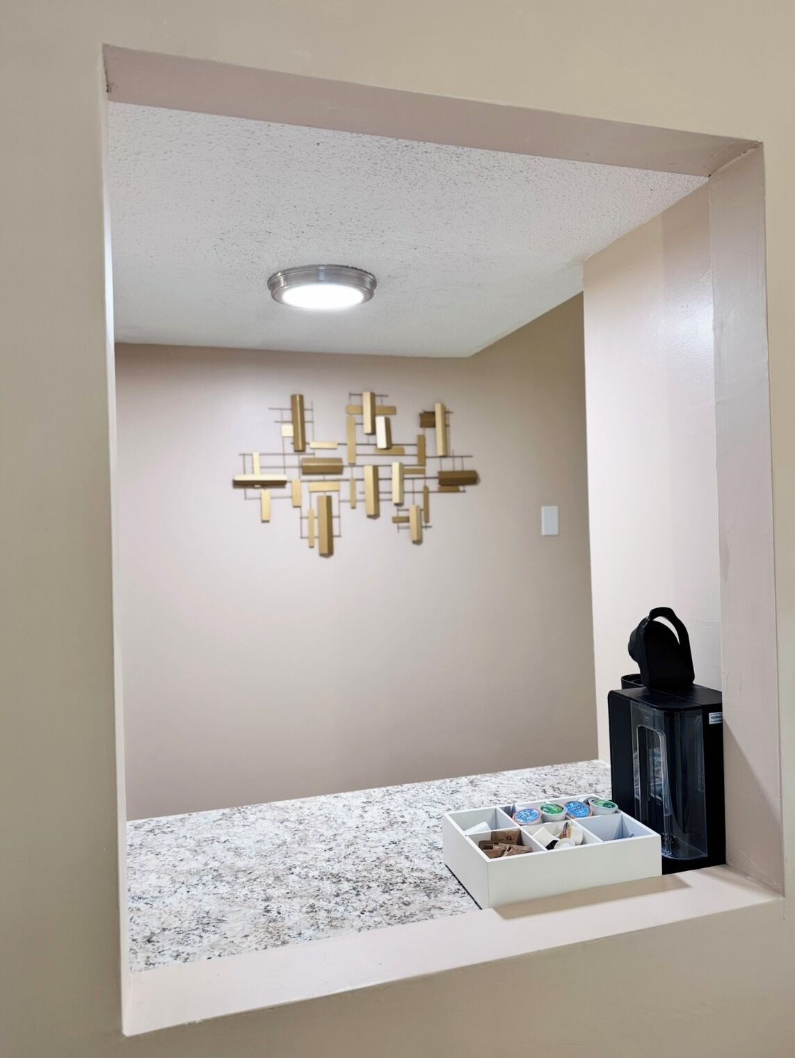 A kitchenette with a marble countertop, a coffee machine, and a decorative wall piece.