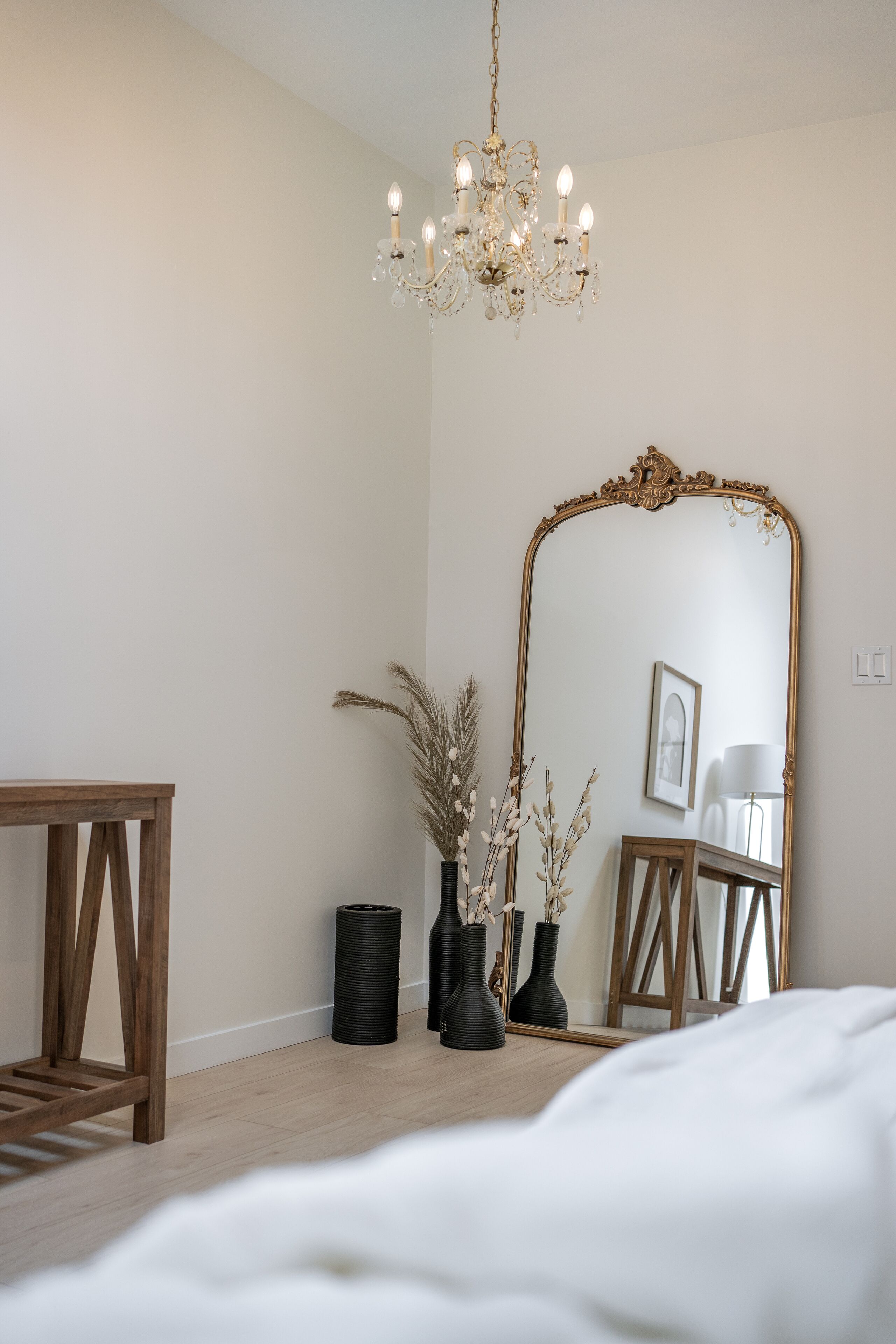 Une chambre à coucher avec un lit en bois, un grand miroir, un lustre et des vases décoratifs.