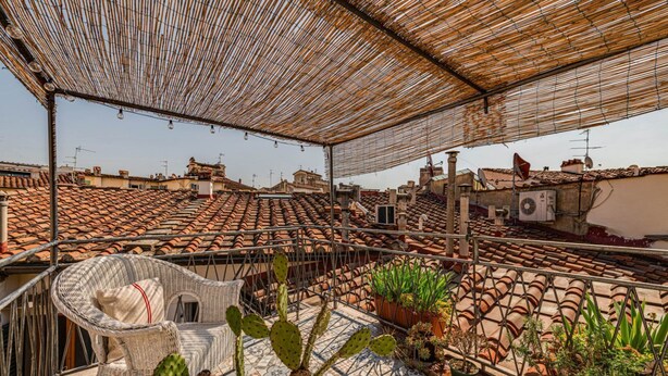 A rooftop terrace with a wicker chair, potted plants, and terracotta roof tiles. - Apartments Florence - Sprone Terrace (Firenze)