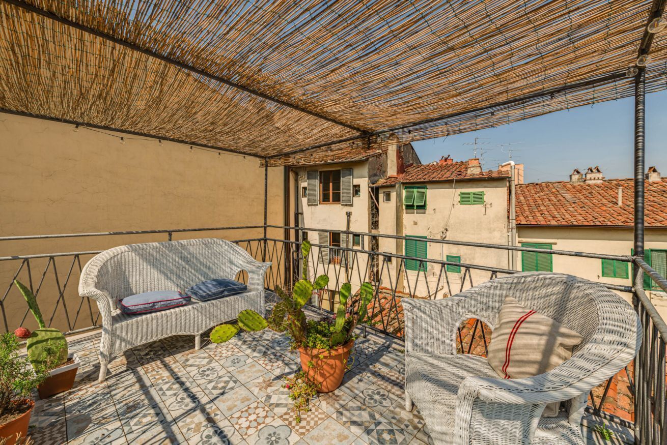 A balcony with wicker furniture, a potted plant, and a tiled floor.