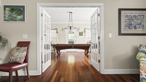 Un pasillo con piso de madera, una mesa de billar y una puerta que da a otra habitación.