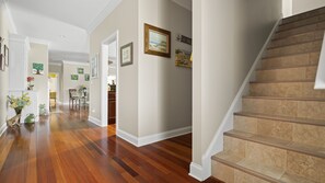 Un pasillo espacioso con pisos de madera, una escalera con baldosas color beige y varias obras de arte enmarcadas en las paredes.