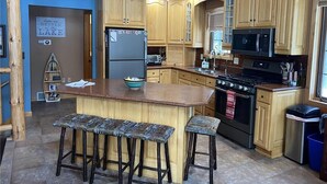 A kitchen with wooden cabinets, a central island with stools, a refrigerator, a microwave, and a stove. - Little Cottage On Prairie - Prairie Lake That Is!!! (Cameron)