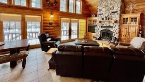 A log cabin interior with a stone fireplace, leather furniture, and large windows. - Little Cottage On Prairie - Prairie Lake That Is!!! (Cameron)