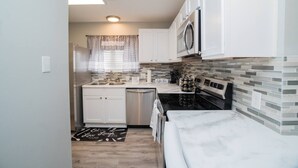 Una cocina pequeña con armarios blancos, estufa negra y salpicadero de azulejos.