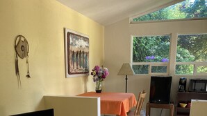 A living room with a TV, sofa, and dining area with a table and chairs. - Lovely two-bedroom garden suite near Willamette River bike path (Eugene)
