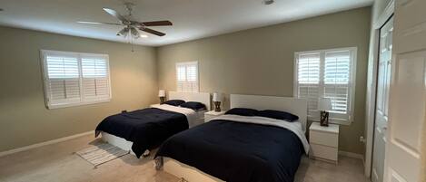 A bedroom with two beds, a ceiling fan, and windows with blinds.