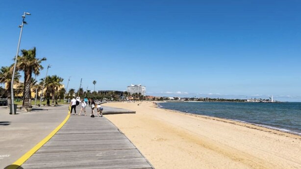 A beach with a wooden boardwalk, palm trees, and a distant building. - NO DISPONIBLE LA CASA. (St. Cloud)