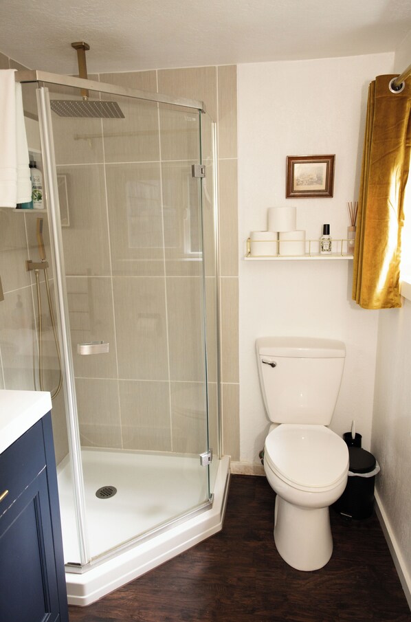 A bathroom with a glass-enclosed shower, a toilet, and a shelf with toiletries. - Deer Meadow Estate at Bandon Dunes - 5-star living (Bandon)
