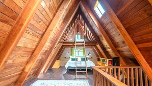 Un dormitorio de ático con piso de madera, con una escalera que lleva a una cama elevada, un escritorio pequeño y una ventana con cortinas.