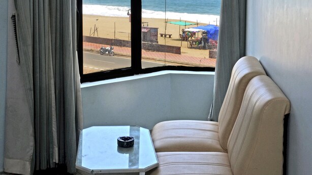 Et værelse med et stort vindue der kigger ud over en strand, en beige sofa og et lille bord med en fjernbetjening.