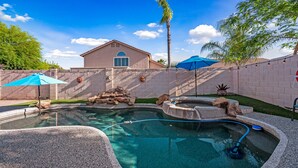 A swimming pool with a stone edge, a house in the background, and a palm tree. - Rose Garden Paradise (Peoria)
