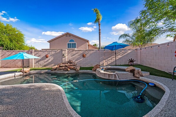 A swimming pool with a stone edge, a house in the background, and a palm tree.