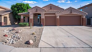 A residential house with a garage, a driveway, and a landscaped garden with rocks and a cactus. - Rose Garden Paradise (Peoria)