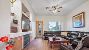 A spacious living room with a fireplace, leather sofas, a wooden coffee table, and a ceiling fan. - Rose Garden Paradise (Peoria)