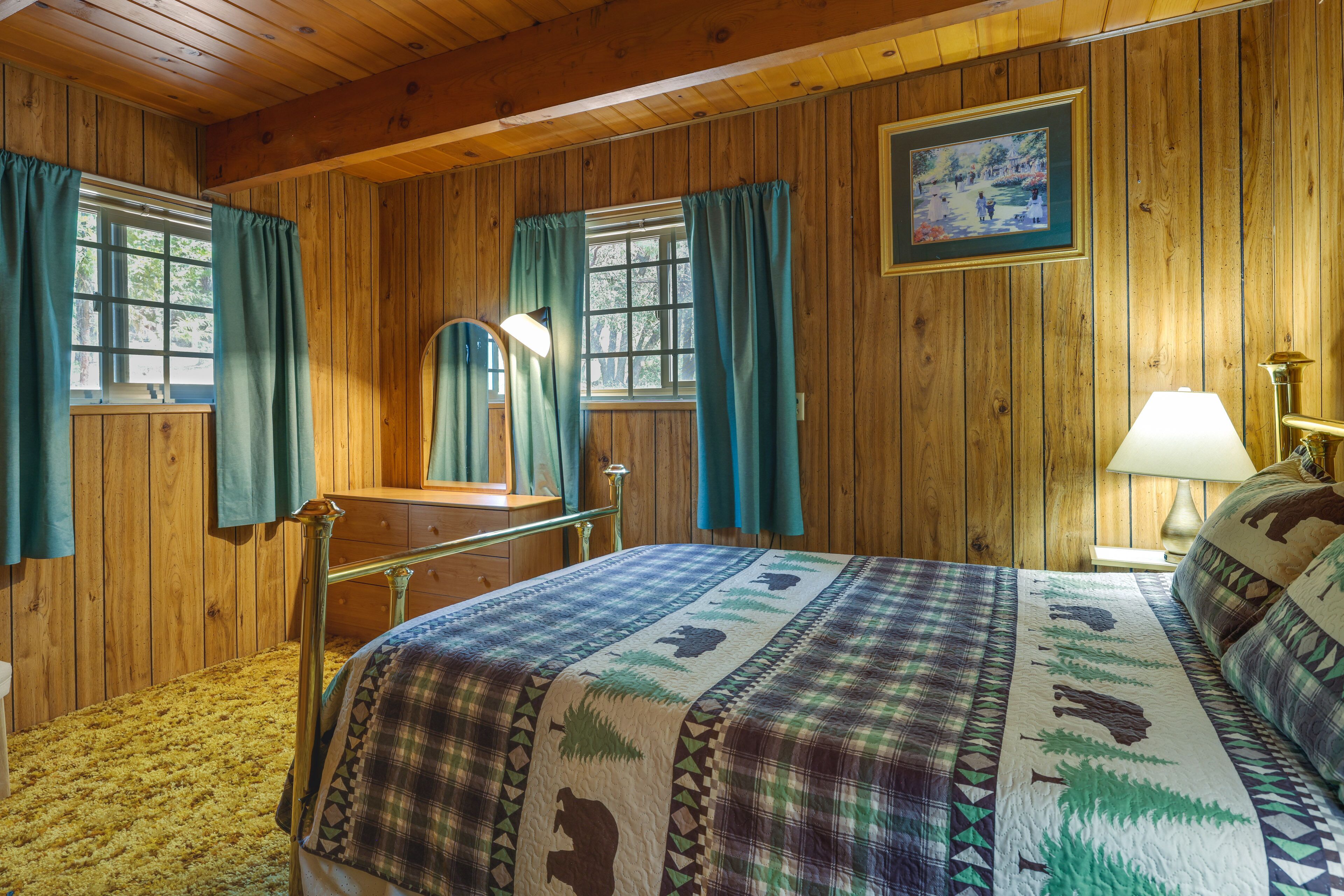 A wooden-paneled room with a bed, a dresser, a mirror, and a window with curtains.