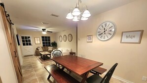 A dining area with a wooden table and benches, a clock on the wall, and a ceiling fan. - Fatima’s Farmhouse: Sleeps8! 4Bd/2Bth/Parking (Jacksonville)