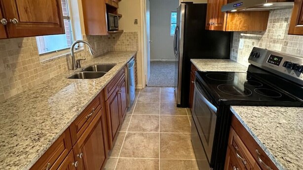A kitchen with wooden cabinets, granite countertops, a stainless steel sink, a black refrigerator, and a stove. - Fatima’s Farmhouse: Sleeps8! 4Bd/2Bth/Parking (Jacksonville)