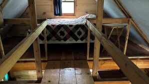 Ein Schlafzimmer im Spitzboden mit Holzboden, einem Stockbett, einem kleinen Fenster mit Vorhängen und Holzbalken.