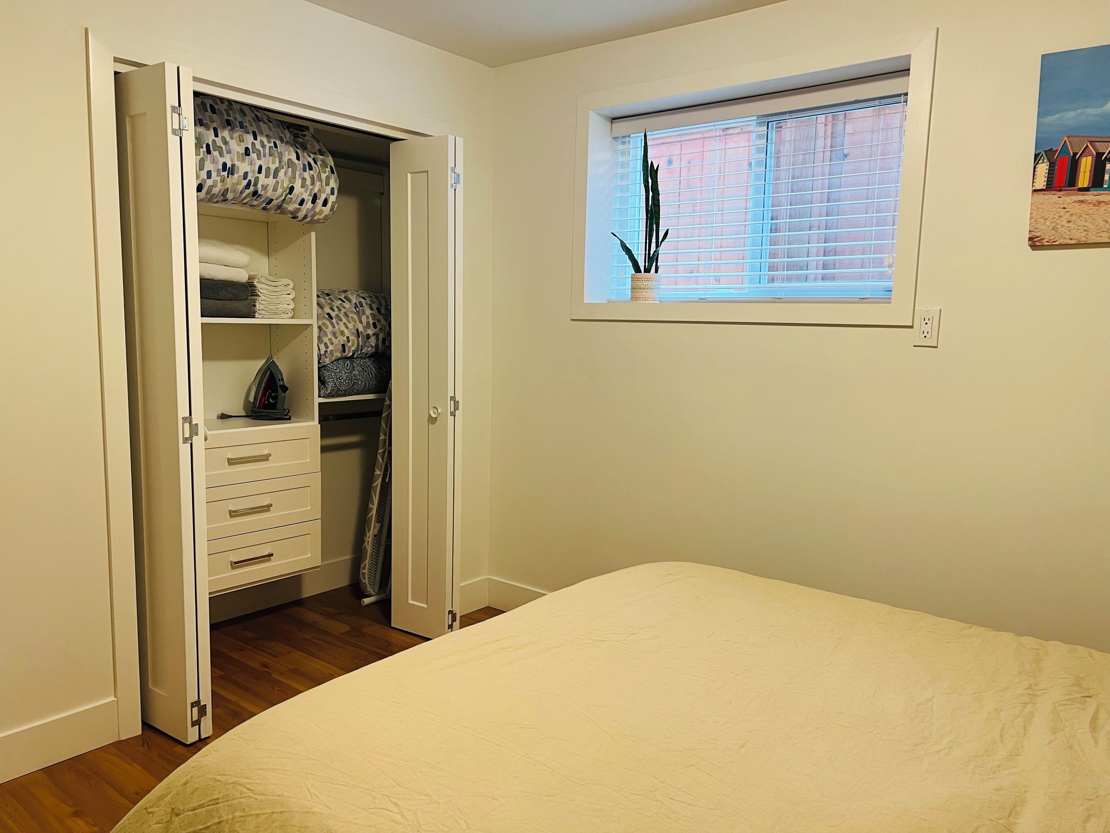 Une chambre à coucher avec un lit, une armoire contenant des serviettes pliées et une fenêtre avec des stores.