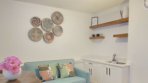 Une cuisine moderne avec des meubles blancs, un évier et un plan de travail en bois. On y trouve un canapé turquoise agrémenté de coussins à motifs et un vase de fleurs posé sur une table en bois.
