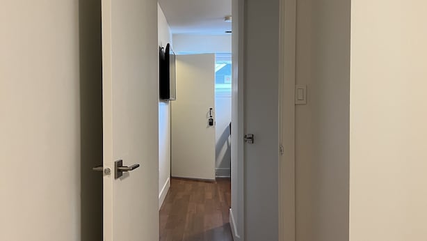 Un couloir doté d’un plancher en bois, de murs blancs et d’une porte donnant sur une autre pièce.