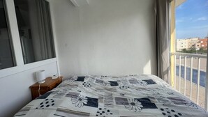A balcony with a bed, a window, and a view of buildings. - AGREABLE DEUX PIECES RENOVE DANS UNE RESIDENCE AVEC PISCINE (LE CAP D AGDE)