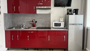 A compact kitchen with red cabinets, a microwave, a coffee maker, and a TV mounted above the counter. - AGREABLE DEUX PIECES RENOVE DANS UNE RESIDENCE AVEC PISCINE (LE CAP D AGDE)