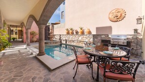 Un espace piscine doté d’un sol en pierre, d’une table ronde avec des chaises et d’un barbecue.