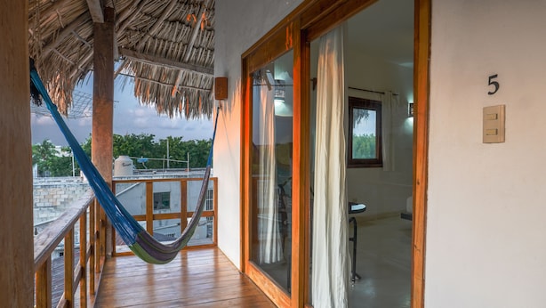 Une terrasse en bois avec un hamac, une porte vitrée donnant accès à une salle de bain et le chiffre « 5 » peint sur le mur.