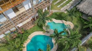 Vue aérienne d’un complexe hôtelier doté de deux piscines, entouré de palmiers et agrémenté d’une terrasse en bois.