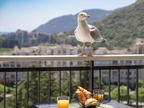 A seagull on a balcony with a table containing a glass of orange juice, croissants, and a basket of bread. - Elegant Studio With Marina Sea And Esterel View (Mandelieu-la-Napoule)