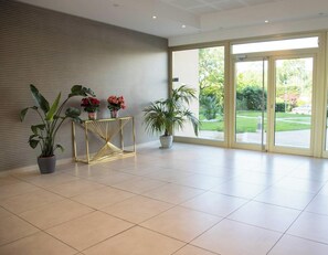 A spacious lobby with a modern design, featuring a tiled floor, a reception desk with potted plants, and large glass doors leading to an outdoor area. - Elegant Studio With Marina Sea And Esterel View (Mandelieu-la-Napoule)