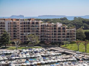 A multi-story residential building with balconies, a marina with numerous boats, and a clear view of the sea and distant land. - Elegant Studio With Marina Sea And Esterel View (Mandelieu-la-Napoule)