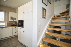 Una cocina con armarios blancos, un microondas y una escalera de madera.