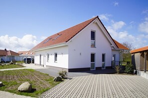 Ein einstöckiges Haus mit rotem Ziegeldach, weißen Außenwänden und einem gepflasterten Auffahrt.