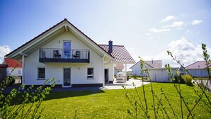 A two-story house with a balcony, a covered patio, and a well-maintained lawn.