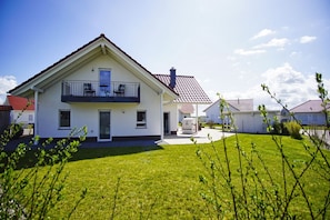 Ein zweistöckiges Haus mit Balkon, überdachter Terrasse und gepflegtem Rasen.