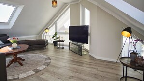 A modern living room with a sloped ceiling, a flat-screen TV, a sofa, a coffee table, and a floor lamp.