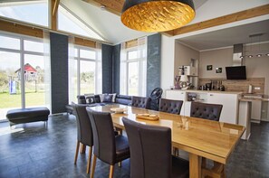 A modern kitchen with a dining area, large windows, and a view of a playground. - Ferienhaus Windrose - Modernes Haus mit Kamin und Eigener Sauna Sowie Garten - Ferienhaus Windrose (Trent)