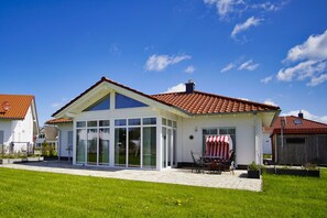 A house with a large glass conservatory, a patio with a table and chairs, and a red and white striped awning.
