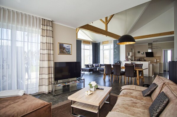 A modern living room with a flat-screen TV, a sofa, a coffee table, and a dining area with chairs and a table.