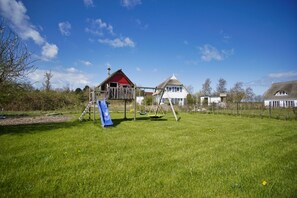 A playground with a slide and swings, surrounded by a grassy field and houses in the background. - Ferienhaus Windrose - Modernes Haus mit Kamin und Eigener Sauna Sowie Garten - Ferienhaus Windrose (Trent)