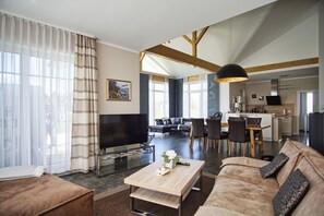 A modern living room with a flat-screen TV, a sofa, a coffee table, and a dining area with chairs and a table.