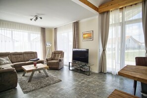 A living room with a sofa, armchair, coffee table, TV, and a dining table. - Ferienhaus Bauernrose - Die Ausstattung vom Ferienhaus Bauernrose (Trent)