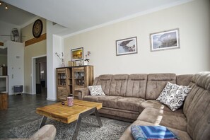 Una sala de estar con un sofá marrón, una mesa de centro de madera y un mueble con puertas de vidrio.