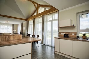 A modern kitchen with a wooden dining table, white cabinets, and a large window providing natural light.