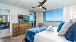 Een slaapkamer met een groot bed, een plafondventilator, uitzicht op de oceaan, een houten kast en een schilderij aan de muur.