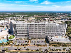 A large hotel with multiple floors, a parking lot, and a swimming pool. - 16th Floor, 5 Pools, Beach Access, Shops Onsite (Panama City Beach)